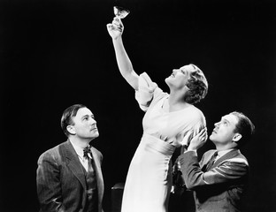 Two men supporting a woman lifting her wine glass 