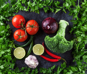 Tomatoes, hot chilli peppers, garlic, onion, lime, and broccoli framed with parsley on grunge background. Top view.