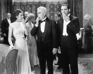 Three people standing together at a formal party yawning and being bored 