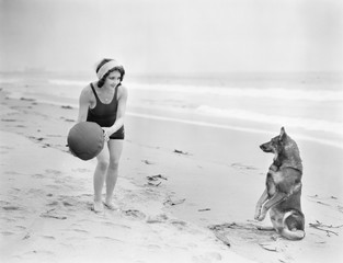 Young woman playing with her dog and ball on the beach 