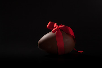 Large chocolate easter egg with red ribbon tied in a bow round it