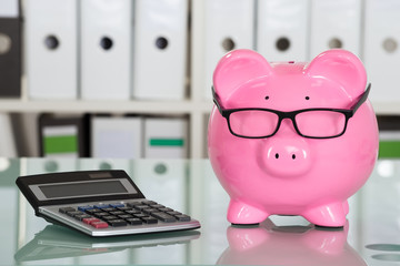 Piggybank Wearing Eyeglasses And Calculator On Desk - obrazy, fototapety, plakaty