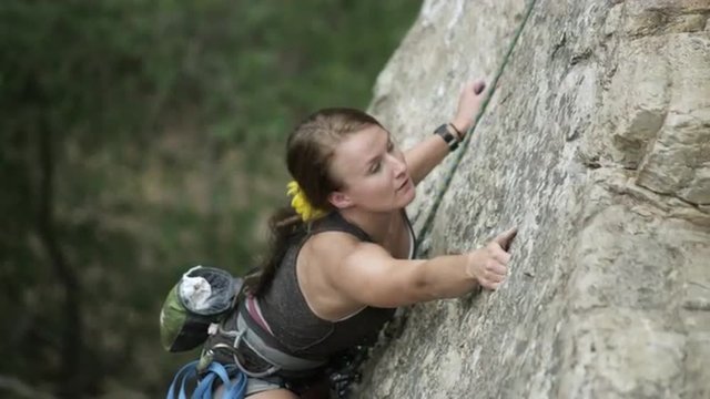 Rock climbing young woman chalking her fingers as she ascends mountain rocky wall.