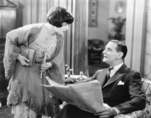 Woman bending over to talk to a man holding a newspaper 