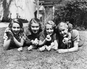 Four young women lying outside with baby chicks. 