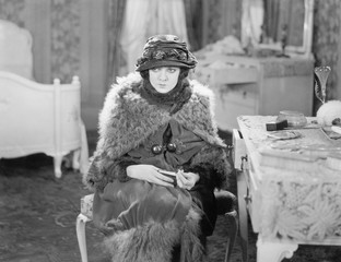 Woman sitting all dressed up in her bedroom looking dejected 