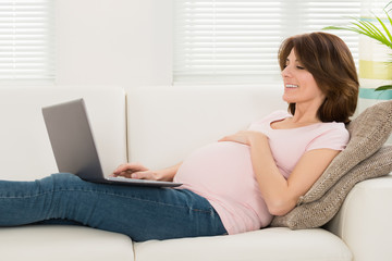 Obraz na płótnie Canvas Pregnant Woman Relaxing On Sofa With Her Laptop