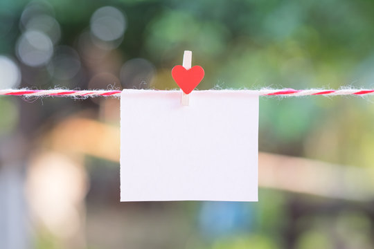 Blank white paper and red clip paper heart hanging on the clothesline with bokeh nature background.Designer concept.