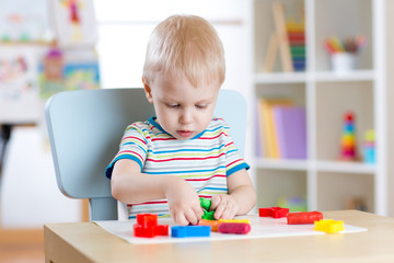 Little boy learning to use colorful play dough in nursery room