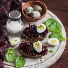 Beetroot relish and a sandwich with beets, quail egg and spinach on rustic light wooden board. Healthy food