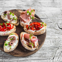 Sandwiches with goat cheese, anchovies, roasted peppers, ham on a wooden rustic board. Delicious snack or appetizer with wine