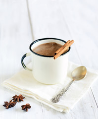 Hot cocoa with cinnamon sticks on white wooden background, star anise