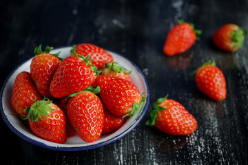 Ripe red strawberries in iron bowl on wooden background