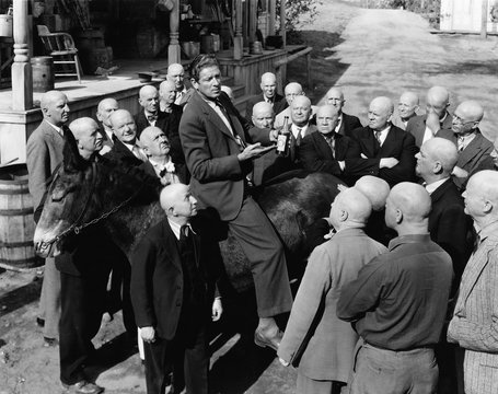 Salesman On Donkey With Group Of Bald Men 