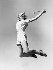 Kobieta skoki w powietrze z rakietą tenisową w ręku - 104455738