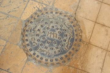 Round hatch in urban tiles road pavement. Arabian relief text on the cap means City Sewerage, North Africa, Cairo, Egypt