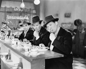 Trzech mężczyzn z czapkami jedzenia w kasie restauracji - 104459583