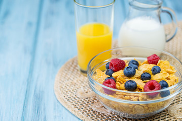 Bowl of cereal with berries, glass of orange juice and jug of milk