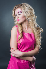 Naklejka premium sexy blonde girl with art makeup posing in the studio on a dark background wall. Pink image. Makeup with flowers.