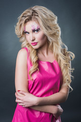 Naklejka premium sexy blonde girl with art makeup posing in the studio on a dark background wall. Pink image. Makeup with flowers.
