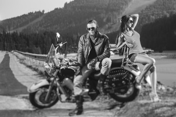 Couple sitting on a motorbike. Handsome man wearing leather jacket, gloves and boots and sexy girl...