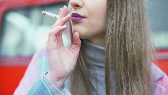 Pretty girl with purple lips sitting and smoking cigarette
