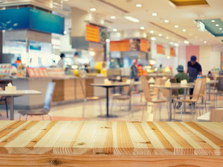 Food court or foodcourt interior blurred background. Restaurant or canteen with table, people at indoor plaza, mall, store or shopping center. Include empty wooden counter or desk for product display.