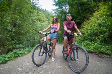 Obraz premium happy couple stays on a mountain road in the woods on bikes looking way
