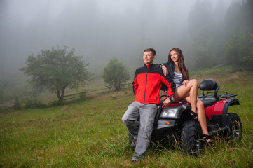 Happy beautiful couple near four-wheeler ATV in foggy nature. Smiling looking into distance