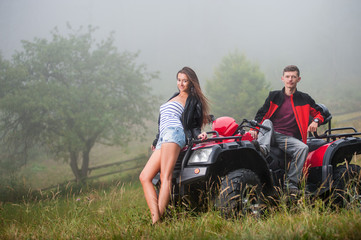 Happy beautiful couple sitting on four-wheeler ATV in foggy nature. Smiling looking at the camera