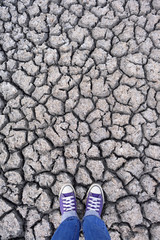 Human legs in sneakers and jeans standing on dried cracked earth