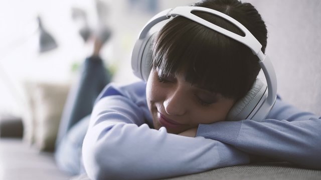 Young woman lying on the sofa, wearing headphones and listening to music, home and entertainment concept