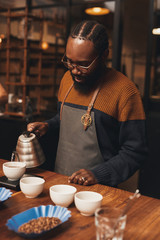 African barista pouring coffee in a modern roastery