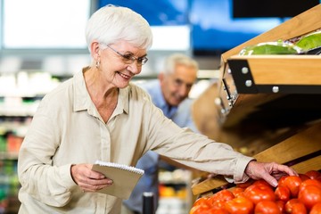 Smiling senior woman with list buying apple