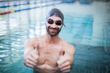 Smiling man wearing swim cap and goggles with thumbs up