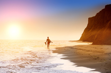 Fototapeta na wymiar Silhouette of a man retreating to the horizon on a deserted beach. Coastline, sea, high cliffs. Sunlight. 