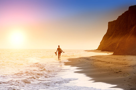 Silhouette of a man retreating to the horizon on a deserted beach. Coastline, sea, high cliffs. Sunlight.
