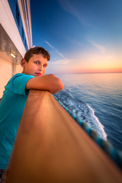 Boy at the railing of a cruise ship at beautiful sunset. 