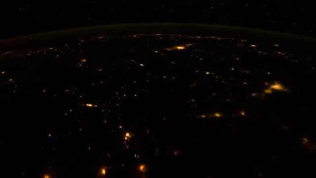 The International Space Station flies over the earth at night with storms and lightning strikes visible.