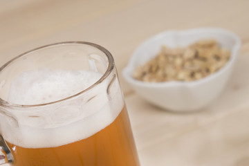 Draft beer and peanuts in the bowl on wood table