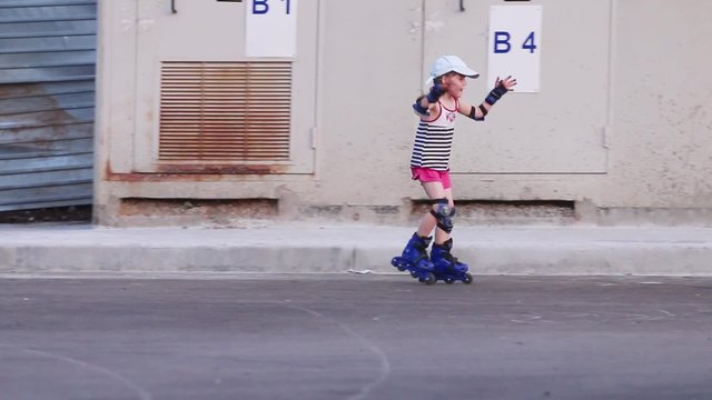 Little girl in cap quickly rides on roller skates on asphalt
