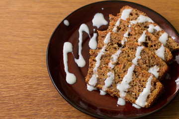Slices of carrot cake with walnuts with cream on brown plate on wood table. 