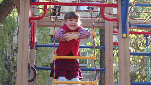 Little girl cheerfully smiles on ladder playground in autumn day