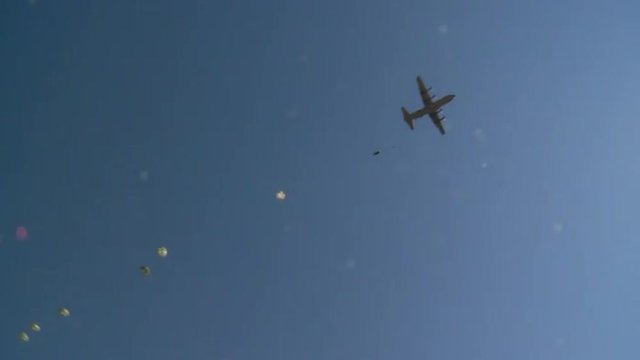 Ground angle view of paratroopers parachuting to earth.