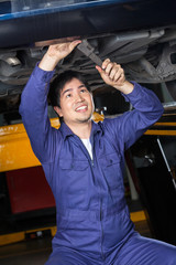 Smiling Mechanic Repairing Underneath Lifted Car