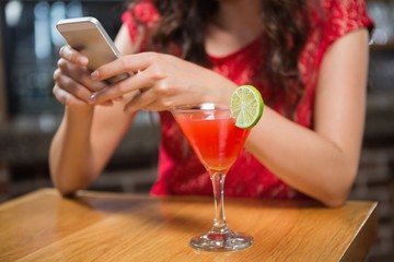 Pretty woman using her smartphone and having a cocktail