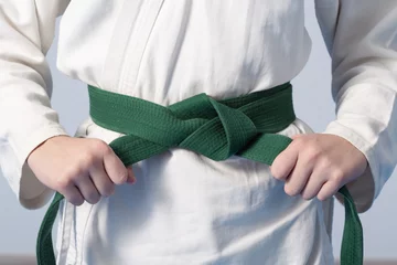 Foto auf Acrylglas Kampfkunst Hands tightening green belt on a teenage dressed in kimono for martial arts
