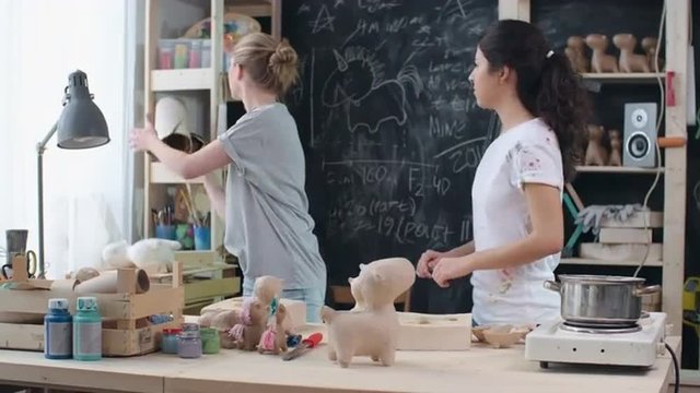Female paper mache artist teaching young woman how to make figures of craft paper at individual workshop 