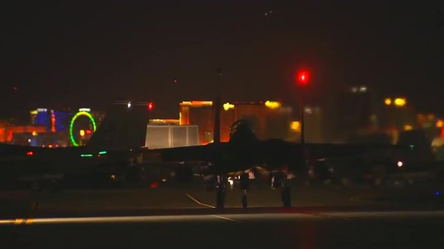 F-15 fighter jets taxis on a runway at night against the Las Vegas skyline.
