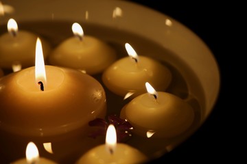 A white bowl with numerous burning candles and a flower in water, big candle in the middle